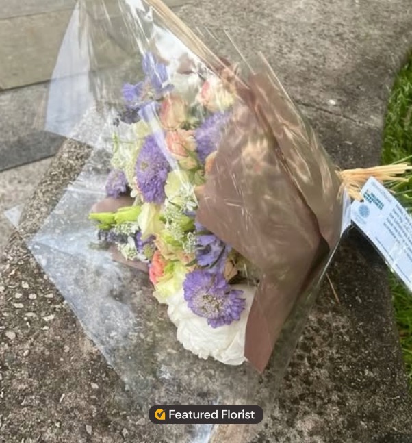 A wrapped Connection Bouquet left on a stone wall by The Little Flowermonger in Rhyl with a note attached for Loneliness Awareness Week.