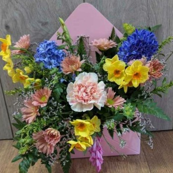 Bespoke spring flower arrangement by local florist featuring daffodils, blue hyacinths, and pink carnations presented inside a pink envelope box wrapper.