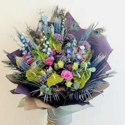 Recent flower delivery by Sarah's Flowers Cheshire featuring pink roses, blue delphiniums, peacock feathers, eucalyptus and seasonal blooms in elegant purple wrapping.