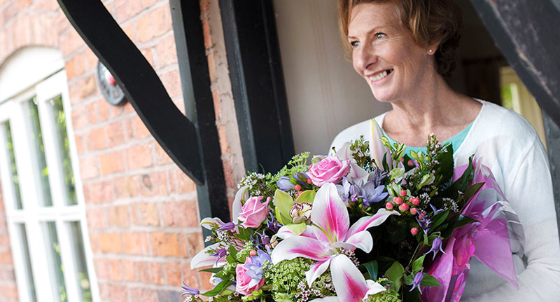 Happy woman stood at front door smiling holding large bouquet