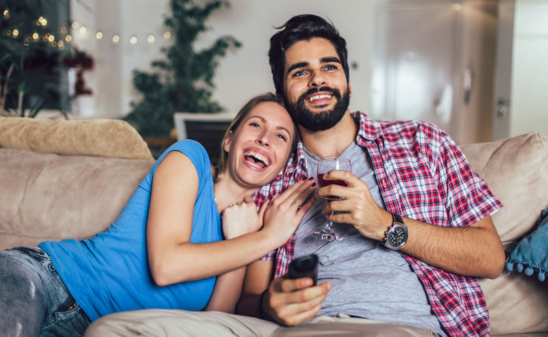 Happy couple relaxing on a couch, watching TV and enjoying a drink