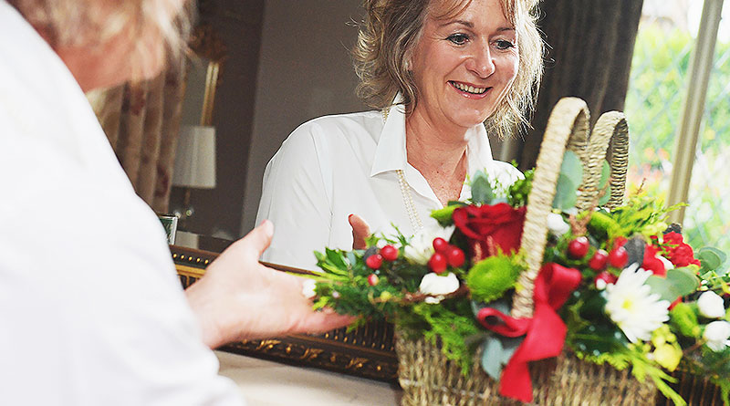 Smiling woman admiring a festive floral basket in a mirror.